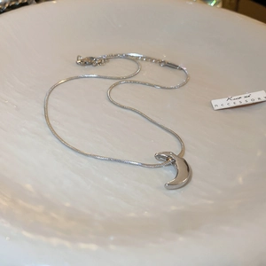 Detail of silver crescent moon necklace on a textured ceramic plate with snake chain
