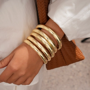 Detailed view of five chunky polished gold-plated geometric bangles worn on the wrist