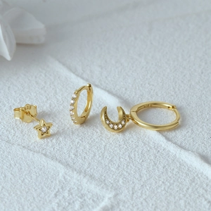Detail of gold 925 silver star and moon earring set with cubic zirconia on white surface