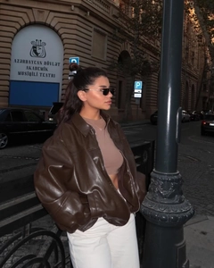 Detail of dark brown faux leather bomber jacket styled with white casual pants