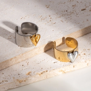 Dettagli di anelli aperti ampi con cuori a contrasto oro e argento su travertino