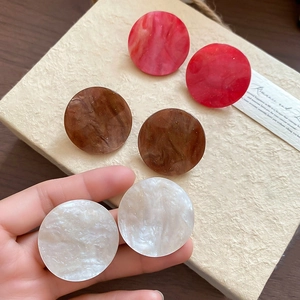 Close-up of geometric acrylic round earrings in red marble, amber brown and cream white