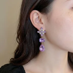 Elegant purple crystal drop earrings with diamond flower top worn by female model