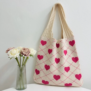 Close-up of beige knitted tote bag with pink heart pattern and rose vase decor