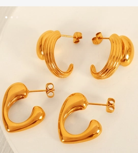 Detail of French style C-shaped gold heart earrings and textured striped hoops