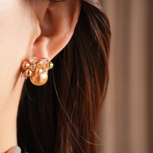 Close-up of a floral gold-plated cluster earring with zircon and pearl on model's ear