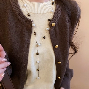 Close-up of vintage Y-shaped necklace with tiger eye stone and pearls on a beige sweater