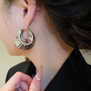 Close-up of chunky silver hoop earrings with geometric grid pattern on a female model