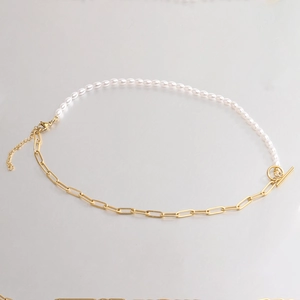 Golden paperclip chain and white pearl necklace with toggle clasp on grey surface