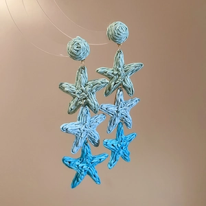 Detailed close-up of blue gradient raffia woven star earrings with fringe tassels