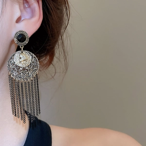 Close-up of vintage tassel earrings with black gem and hollow coin detail on model