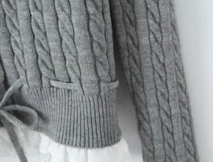 Close-up of grey cable knit sweater featuring delicate white lace trim and waist tie