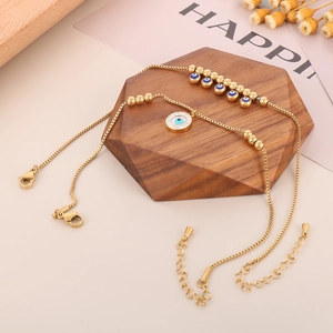 Detail of gold evil eye anklets with blue beads and lobster clasp on a wooden stand