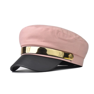 Detailed view of pink fabric baker boy hat with black visor and gold M metal bar