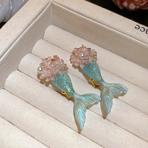 Close-up of glittery teal fishtail hair clips with pearls on a beige velvet jewelry box