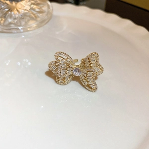 Close-up of golden bow-shaped open ring with micro-set zircons on a textured white plate