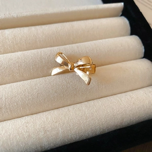 Macro detail of a small golden metal bow hair clip on a beige velvet jewelry box