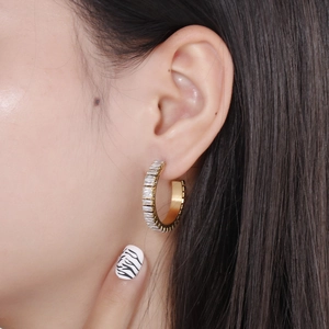 Close-up of gold hoop earrings with baguette-cut white zircons worn by a model