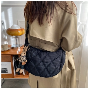 Detail of black quilted dumpling bag with bunny plush charm on beige trench coat