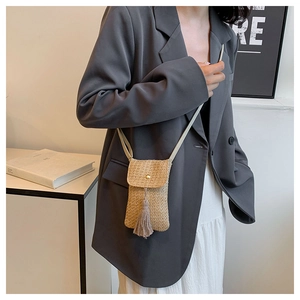 Detail of beige straw woven crossbody phone bag with fringe and metal snap on a grey blazer