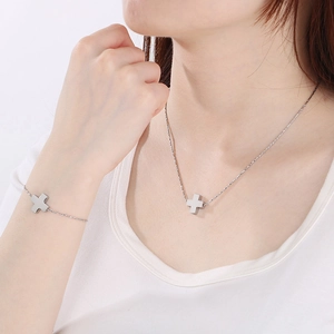 Close-up of a silver stainless steel cross necklace and bracelet set worn by a model