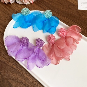 Detailed macro of organza fabric flower earrings with beaded stamens in a ceramic tray