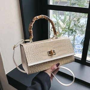 Close-up of beige crocodile pattern bag with bamboo handle and gold twist lock clasp