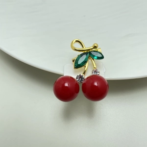 Detailed macro view of cherry brooch with red fruits and green gemstone leaves