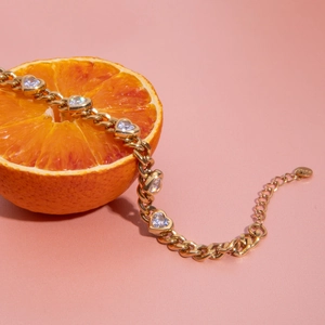 Gold chain bracelet with heart-shaped zircon on an orange, coral pink background