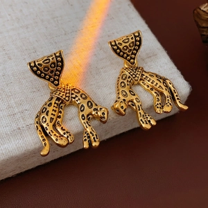Vintage gold leopard drop earrings with leopard print detail on gray display stand