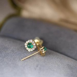 Macro detail of gold flower earrings featuring emerald center stones and diamond accents