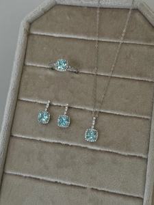 Detail of jewelry set featuring light blue square-cut gemstones and silver halo settings