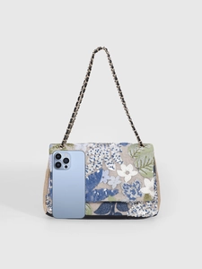 Size comparison of a floral sequin embroidered shoulder bag next to a smartphone