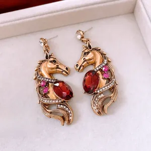 Detail of vintage gold horse earrings with red gemstones on beige jewelry box display