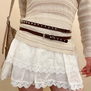 Détail d'une ceinture en cuir marron avec rivets sur une jupe en dentelle et haut tricot