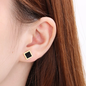 Close-up of minimalist square gold earrings with black center worn on a model ear