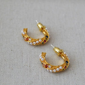 Gold twist hoop earrings with colorful zircon and pearl accents on gray texture