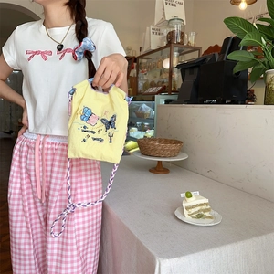 Détail d'un mini sac en toile jaune avec broderie papillon et bandoulière tressée