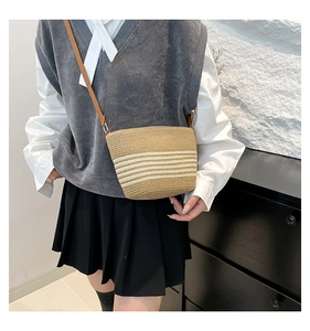 Detail of khaki striped straw bucket bag with adjustable strap worn by a female model