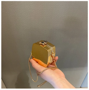 Close-up of golden metallic mini box bag with sleek snake chain held in hand