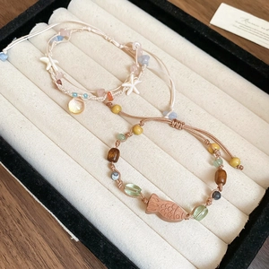 Details von gewebten Armbändern mit bunten Natursteinen und Seesternen auf einem Samttablett