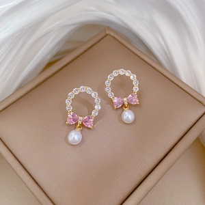 Detail of gold bow earrings featuring pink zircon, crystal ring, and hanging white pearl