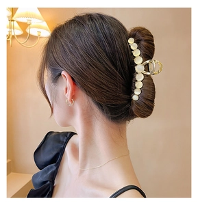 Détail d'une pince à cheveux en métal doré avec opales portée sur un chignon de femme