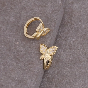 Macro detail of gold butterfly hoop earrings with sparkling cubic zirconia on stone background