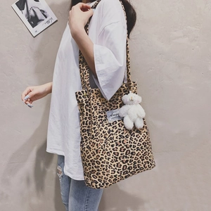 Leopard print canvas tote bag with plush bear charm worn on shoulder by a model