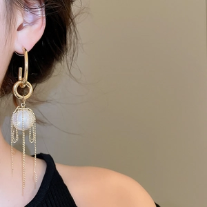 Detail of long gold tassel earrings with large pearls on model in a soft close-up view
