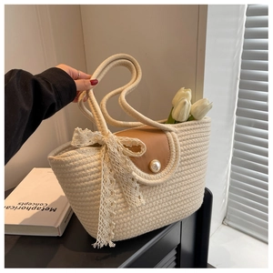 Detailed view of beige straw tote bag with brown leather flap and pearl button lace bow