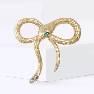 Enamel snake bow brooch in gold metal with green gem eyes on white pedestal