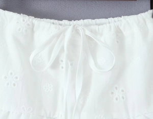 Détail de la broderie anglaise blanche sur coton avec motifs floraux et cordon de serrage à nouer
