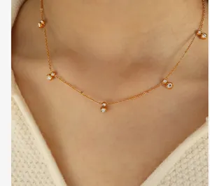 Close-up of minimalist gold necklace with five bezel-set cubic zirconia on white knitwear